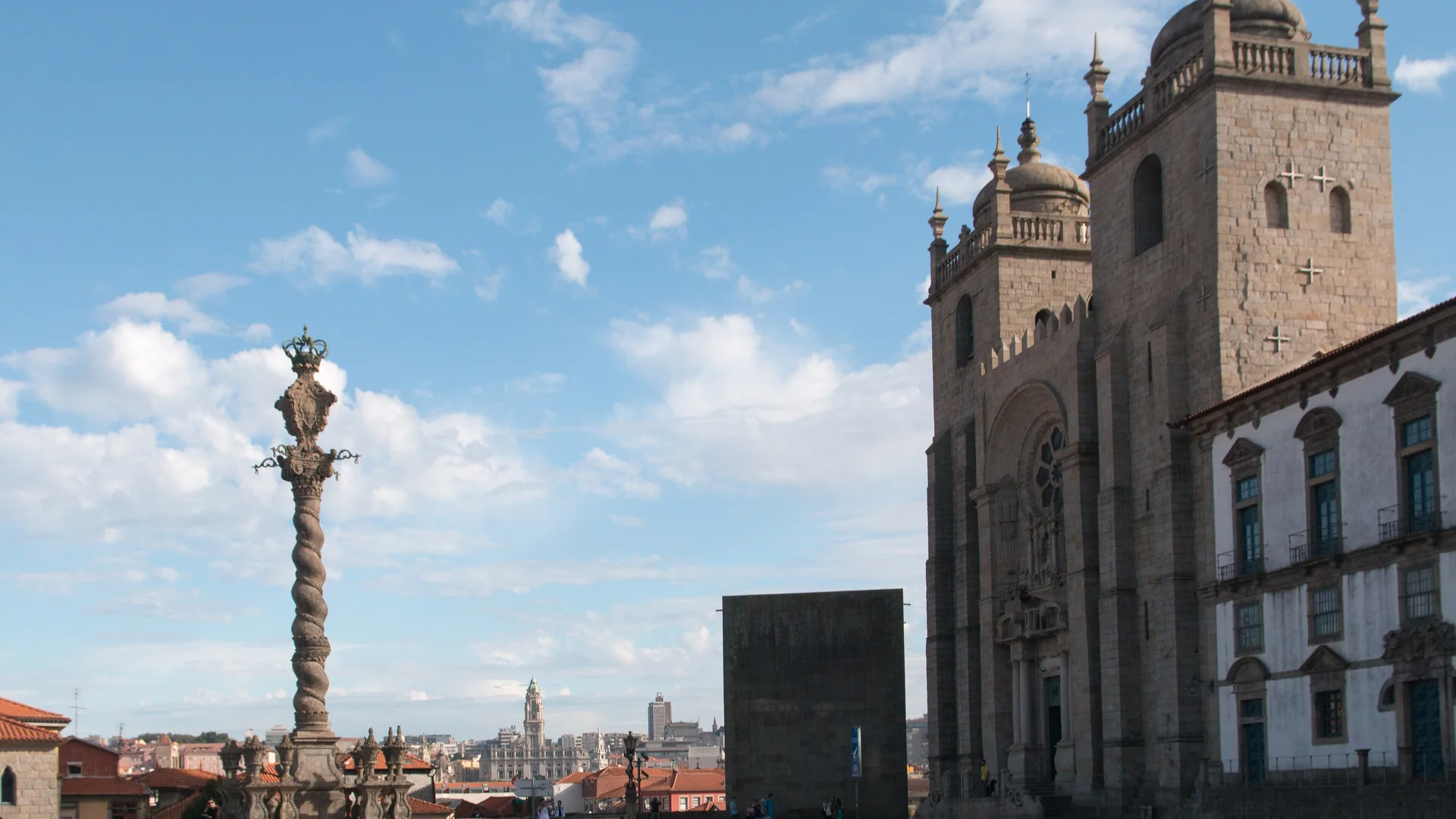 La Cattedrale di Porto e la sua piazza sotto un cielo azzurro, con la colonna di pietra della berlina a sinistra e le due torri della cattedrale a destra.