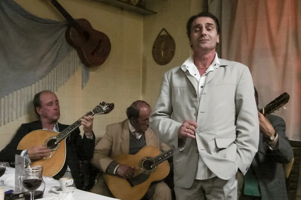 Una cantante di fado in abito chiaro accanto a due chitarristi seduti in una piccola sala di Porto.