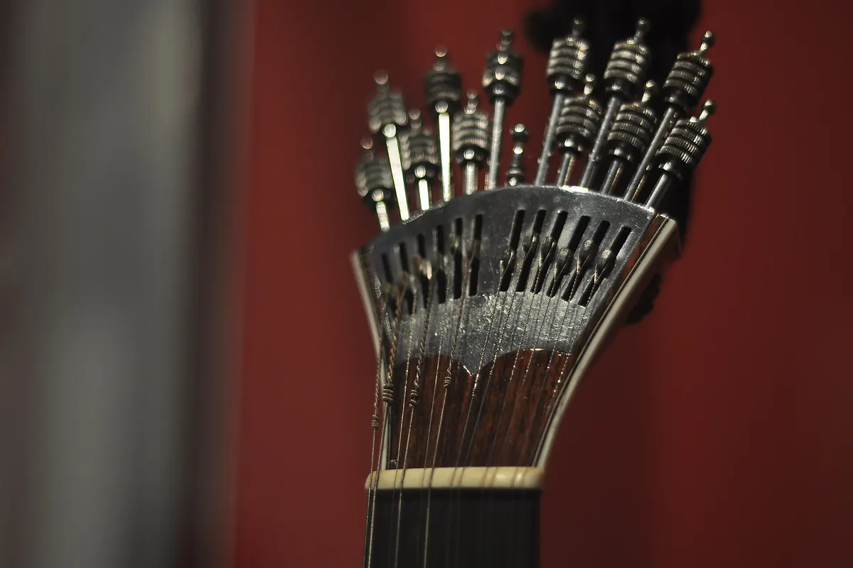 Il meccanismo di accordatura in metallo a ventaglio di una chitarra portoghese con la sua fila di chiavi, su sfondo rosso.